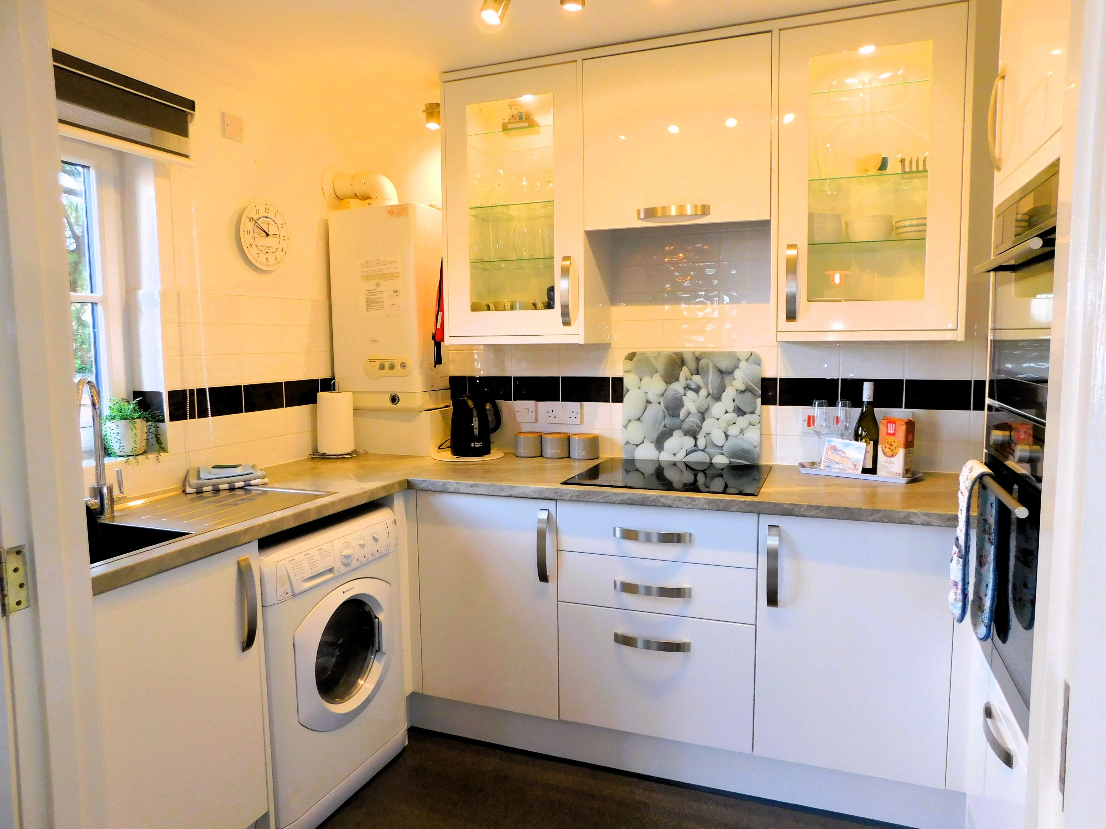 A modern kitchen with a built-in washing machine, a coffee maker, and a glass display cabinet.