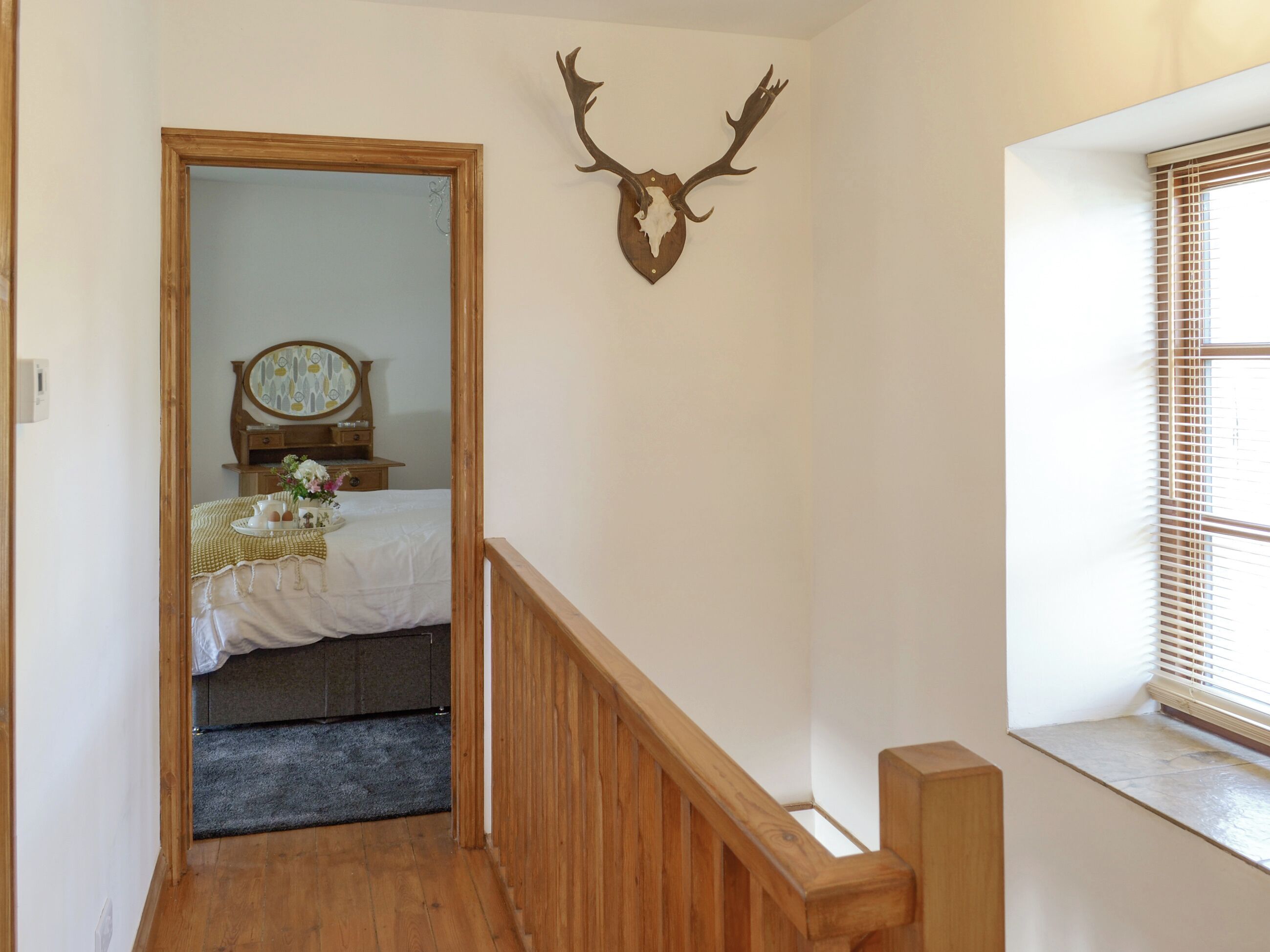 A bedroom with a wooden bed, a bedside table, a mirror, and a deer head mounted on the wall.