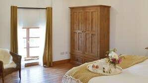 Ein Zimmer mit einem Holzkleiderkasten, einem Korbstuhl, einem Bett mit weißer Bettdecke, einem Tablett mit Frühstücksangeboten und einer Chandelieber.