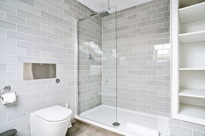 Une salle de bain moderne avec une douche à parois de verre, des carreaux blancs, des toilettes et une étagère.