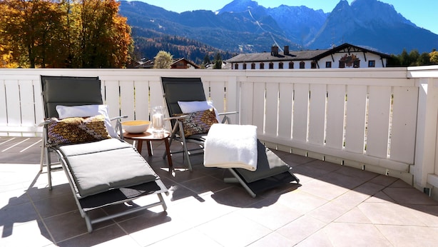 Una terrazza con due poltrone, un tavolino con una ciotola e vista sulle montagne.