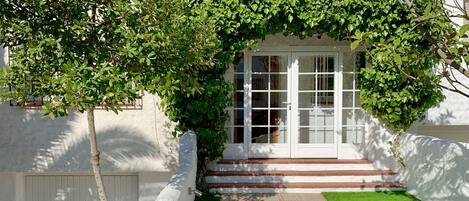 A white building with a glass door entrance, a small front garden, and a number '30' sign.