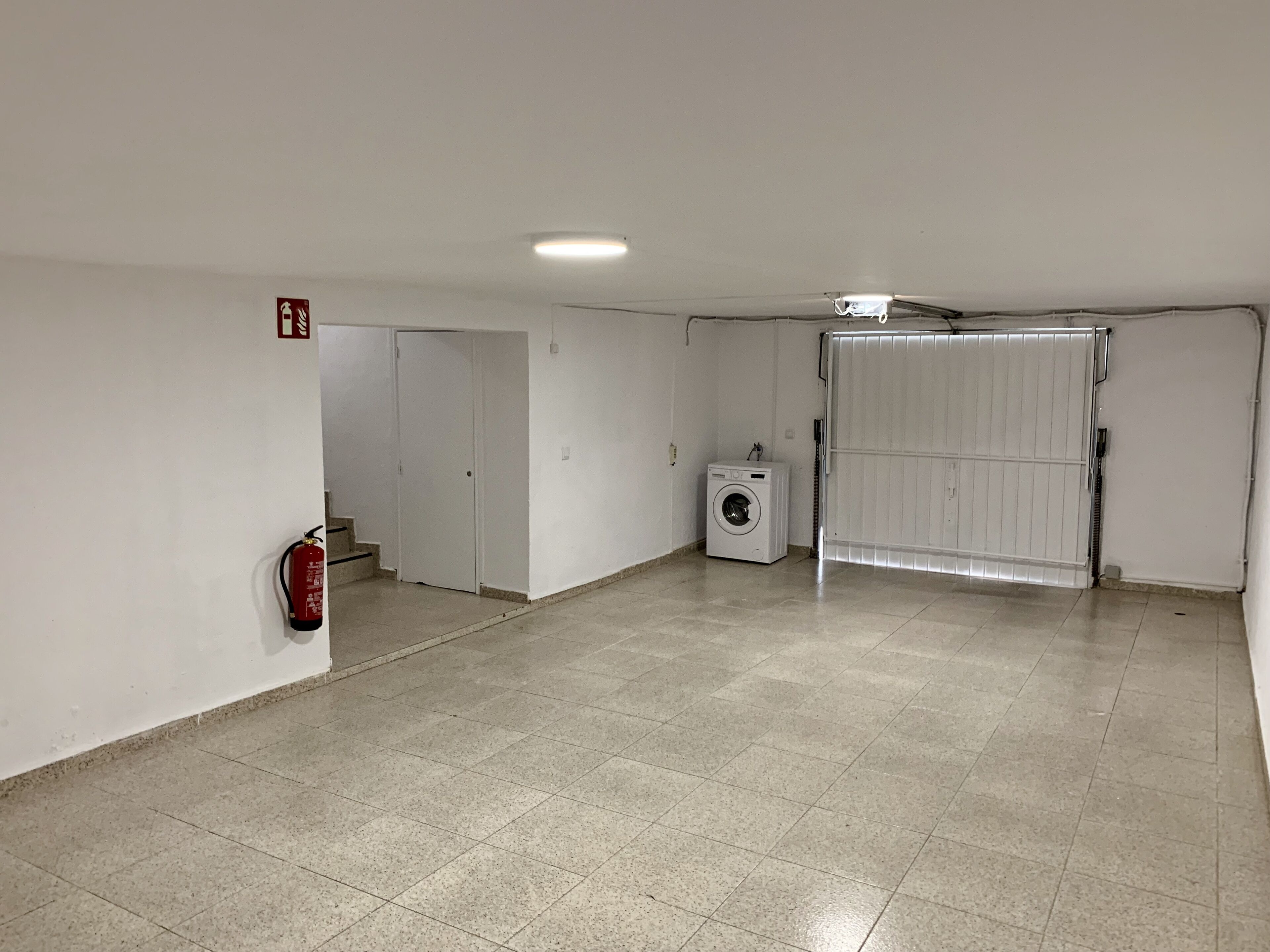 A spacious room with a tiled floor, a washing machine, a fire extinguisher, and a sliding door.