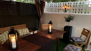 Uma área de estar ao ar livre com uma mesa de madeira, duas cadeiras e duas lanternas.