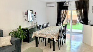 Uma sala de jantar com mesa e cadeiras, um sofá, uma planta em vaso e vista para o exterior.