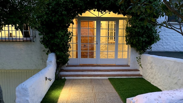 Uma entrada de edifício com um caminho de azulejos que leva a uma porta com painéis de vidro.
