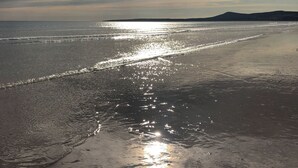 Una playa con un mar tranquilo y una montaña distante.