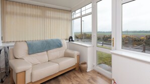 Una habitación con un sofá beige, una ventana que da a un campo y suelo de madera.