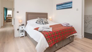 Un dormitorio con cama, lámparas de noche, un cuadro y vista al pasillo.