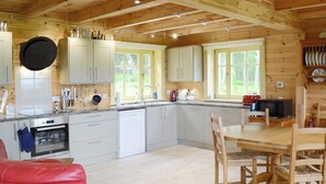 A modern kitchen with white cabinets, a dining area with a wooden table and chairs, and a red leather chair. - 2 bedroom accommodation in Culbokie, near Dingwall (Culbokie, near Dingwall)