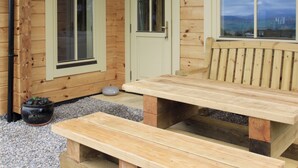 A wooden cabin with two doors and windows, a bench, and a table. - 2 bedroom accommodation in Culbokie, near Dingwall (Culbokie, near Dingwall)