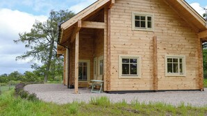 A wooden cabin with a sloped roof, a covered porch, and a gravel driveway. - 2 bedroom accommodation in Culbokie, near Dingwall (Culbokie, near Dingwall)