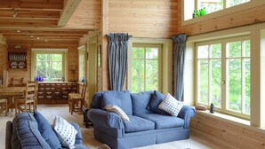 A cozy cabin interior with a blue sofa set, a dining area, and large windows offering a view of the greenery outside. - 2 bedroom accommodation in Culbokie, near Dingwall (Culbokie, near Dingwall)