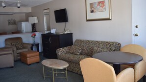 A furnished living room with a sofa, armchairs, a small round table, a coffee table, a TV, a refrigerator, and a cabinet. - Cullars Inn (Lincolnton)