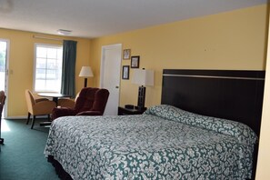 A hotel room with a large bed, a desk with a chair, a lamp, and a window with curtains.