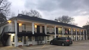 A two-story motel with a central entrance, a covered outdoor seating area, and a parking lot. - Cullars Inn (Lincolnton)