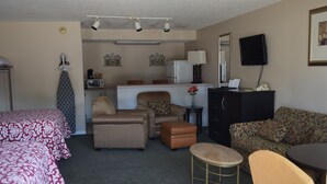 A hotel room with a bed, two sofas, a small table, a cabinet, a microwave, a refrigerator, a television, and a mirror. - Cullars Inn (Lincolnton)