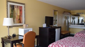 A hotel room with a desk, chair, bed, and a large mirror. - Cullars Inn (Lincolnton)