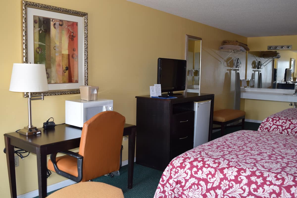 A hotel room with a desk, chair, bed, and a large mirror.