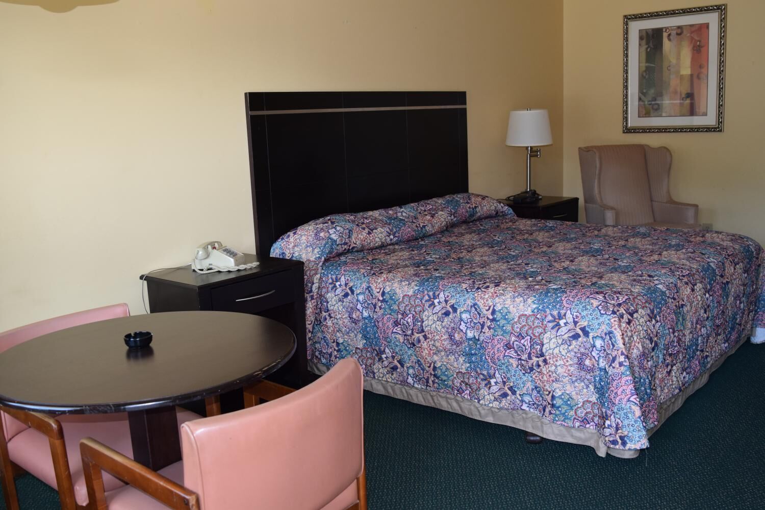 A hotel room with a bed, a desk with a telephone, a chair, and a lamp.