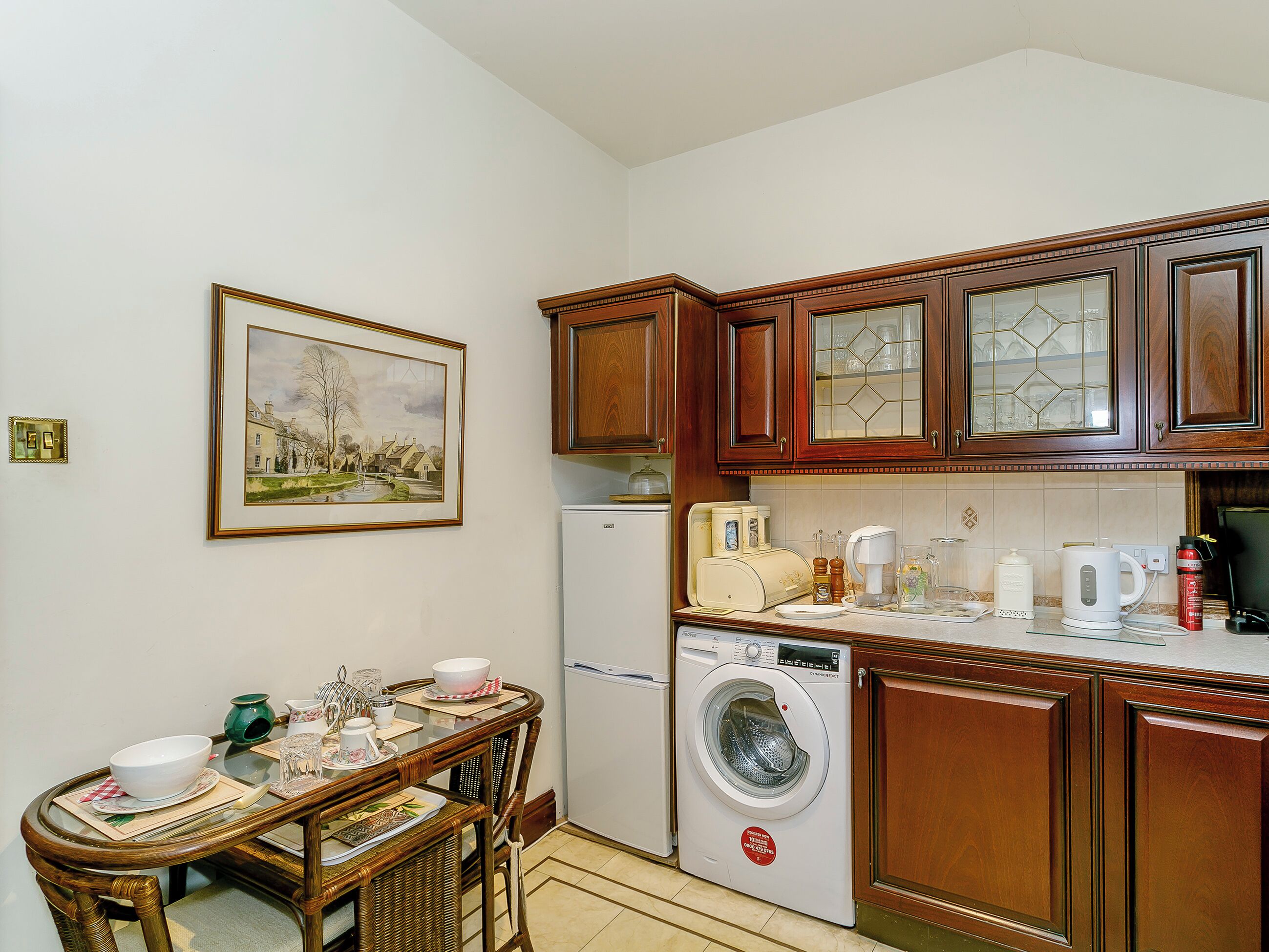 A compact kitchen with wooden cabinets, a washing machine, and a dining area with a table and chairs.