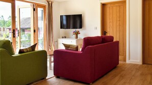 A living room with a green sofa, a red sofa, a flat-screen TV, and a wooden door. - 2 bedroom accommodation in Canon Frome, near Ledbury (Canon Frome, near Ledbury)
