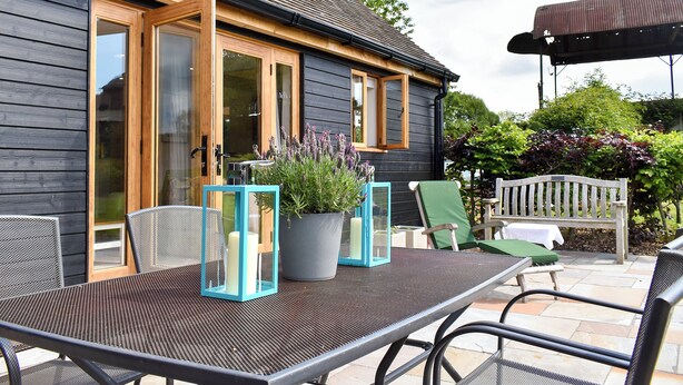 A wooden house with a patio area featuring a table, chairs, and potted plants. - 2 bedroom accommodation in Canon Frome, near Ledbury (Canon Frome, near Ledbury)