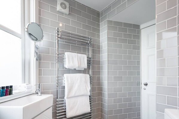 A bathroom with grey tiled walls, a white sink, a mirror, and a towel rack with two white towels. - Unique Flat in the Heart of New Town (Edinburgh)
