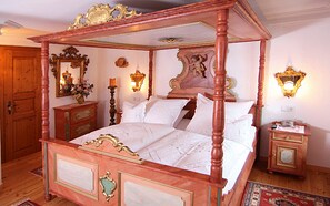 A four-poster bed with ornate carvings, a wooden wardrobe, a mirror, and a nightstand with a lamp.