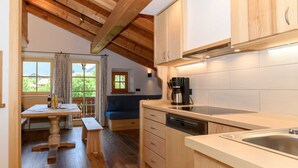 Una cocina con armarios de madera, lavavajillas, cafetera y ventana con vista a la vegetación.