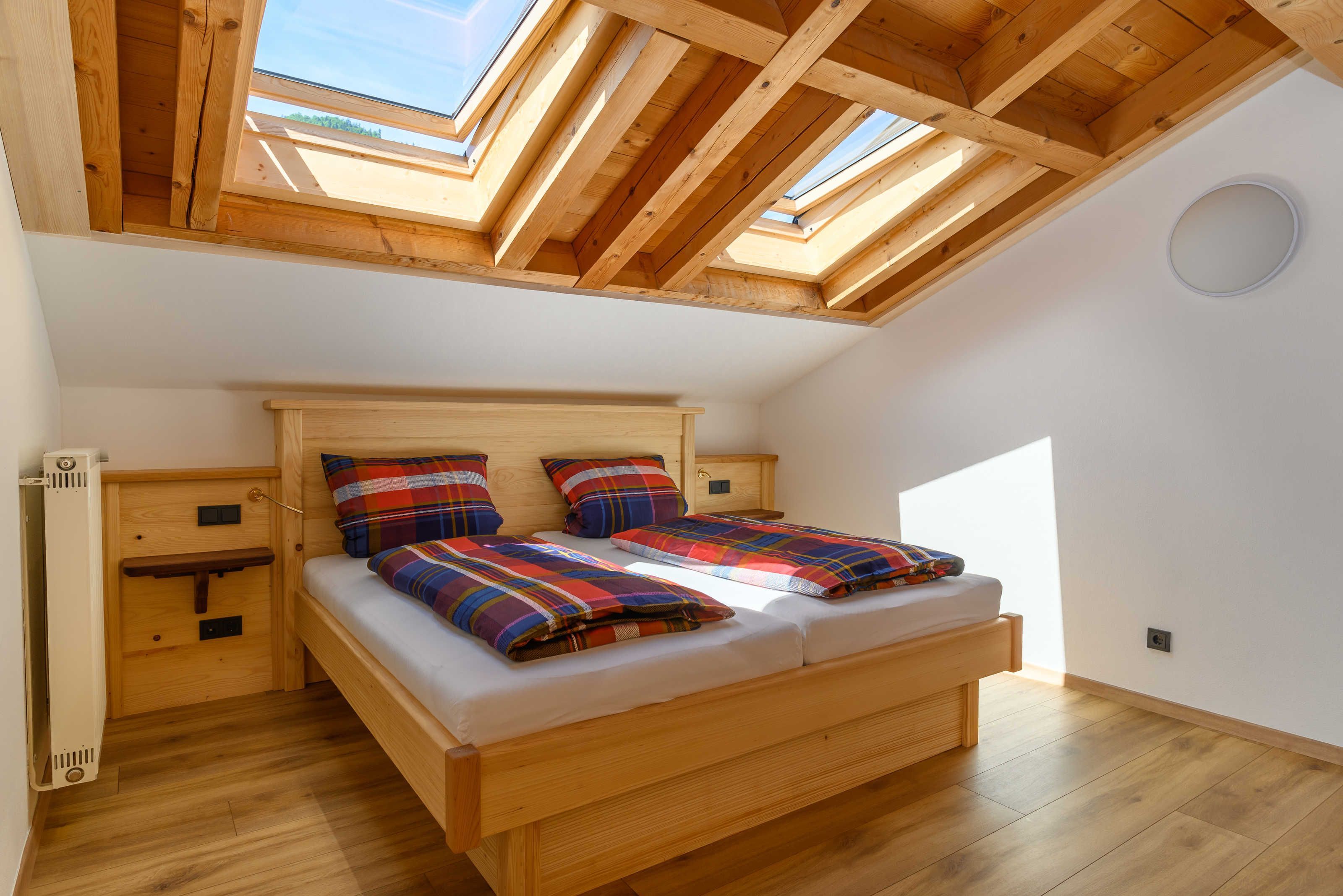 Una habitación con techos altos, un tragaluz, una cama de madera y una mesita de noche pequeña.