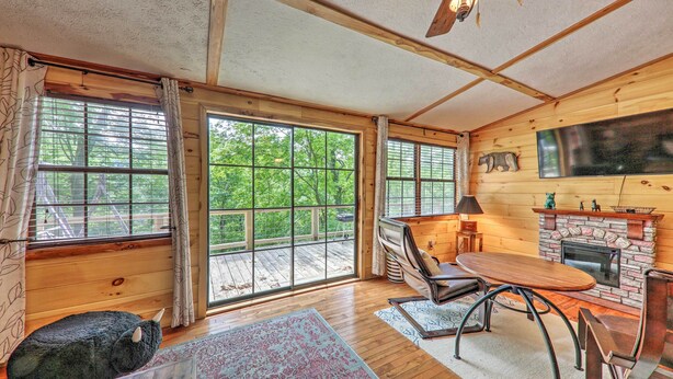 Un interior de cabaña acogedor con ventanas amplias, chimenea, ventilador de techo y un sofá mullido.