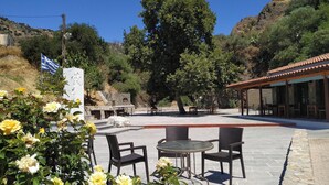 An outdoor seating area with stone flooring, surrounded by greenery and a mountainous backdrop. - Il Silenzio (first floor) Magarikari South Crete (Magarikari)