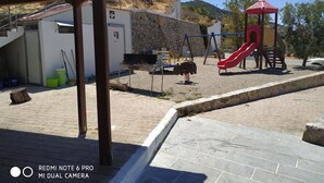 A playground with a red slide and swings, a barbecue area, and a stone wall. - Il Silenzio (first floor) Magarikari South Crete (Magarikari)