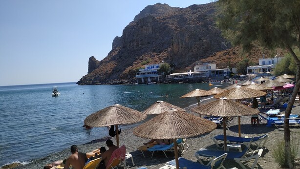 A beach with thatched umbrellas, lounge chairs, and a rocky cliff in the background. - Il Silenzio (first floor) Magarikari South Crete (Magarikari)