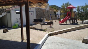 A playground with a red slide and swings, a barbecue area, and a stone wall. - Il Silenzio (first floor) Magarikari South Crete (Magarikari)