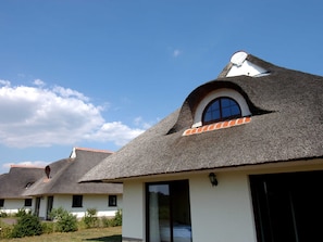 Eine Reihung von Häusern mit strohgedeckten Dächern und weißen Wänden, mit großen Fenstern und blauem Himmel.