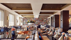 A modern restaurant with high ceilings, a central seating area, and a variety of dining tables and chairs.