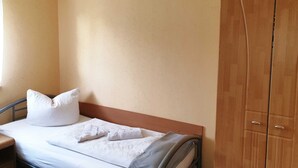 A single bed with white bedding and pillows, a wooden wardrobe, and a window with curtains. - Single room - Pension Henze (Hoyerswerda)