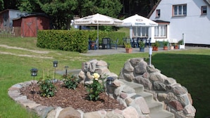Un hotel con mesas al aire libre, un jardín con rosales y un muro de piedra.