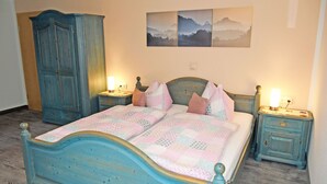 Un dormitorio con una cama azul, dos mesitas de noche con lámparas, un armario y una pared con tres cuadros.