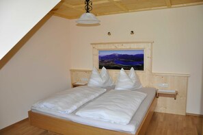 Makuuhuoneessa on puinen sänky, yöpöytä, seinään kiinnitetty lamppu ja kehystetty maisemakuva.
