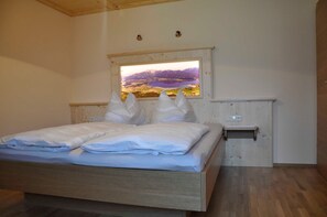 Une chambre avec un lit en bois, une petite table de chevet et une fenêtre donnant sur les montagnes.