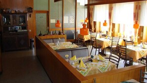 Un restaurante con interior de madera, varias mesas con manteles amarillos y lámparas colgantes naranjas.