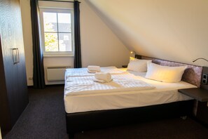 A hotel room with a bed, a nightstand, a lamp, a window with curtains, and a radiator.