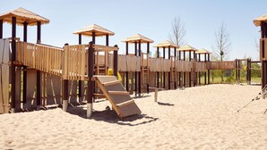 A wooden play structure on a sandy beach with multiple levels and slides.