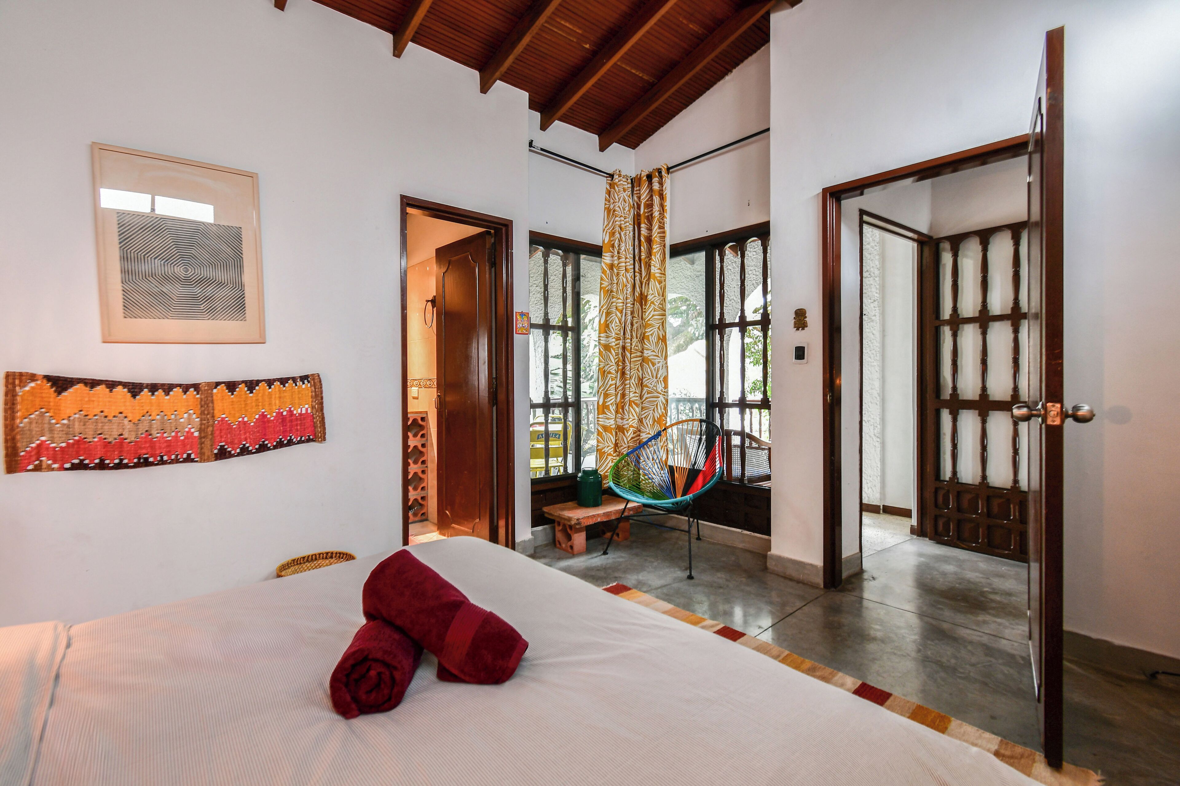 A hotel room with a bed, a bench, a chair, and a view of the outside.