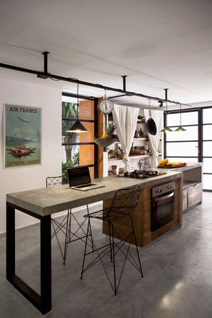 A modern kitchen with a large island, a laptop on the counter, and a poster on the wall.