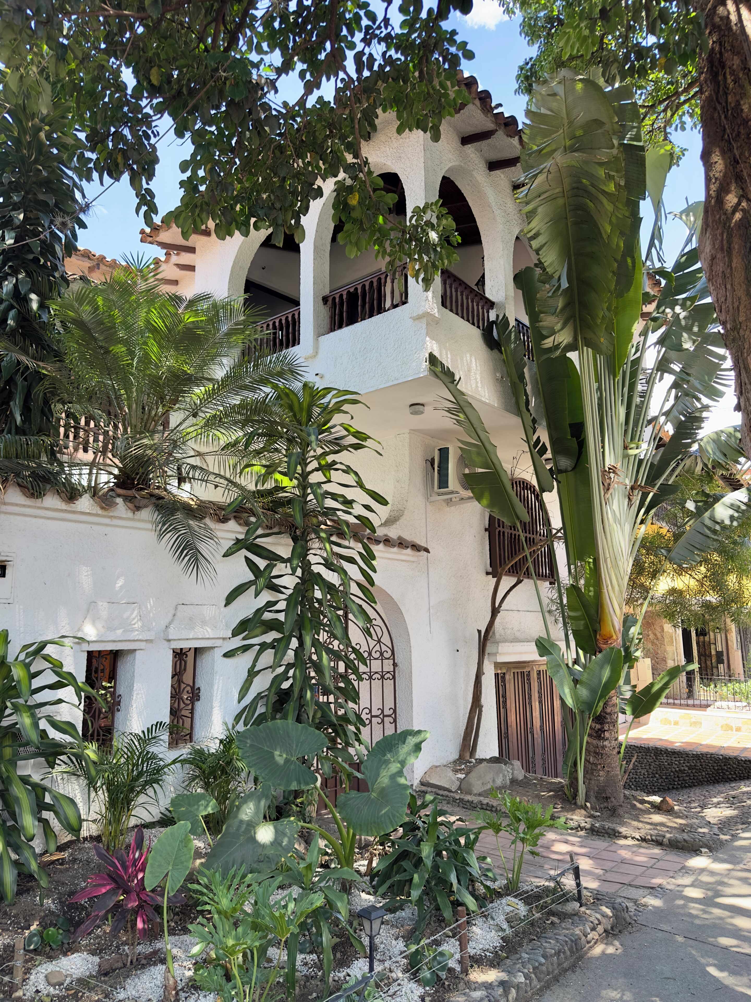 Um edifício com fachada branca, várias varandas e plantas tropicais exuberantes.