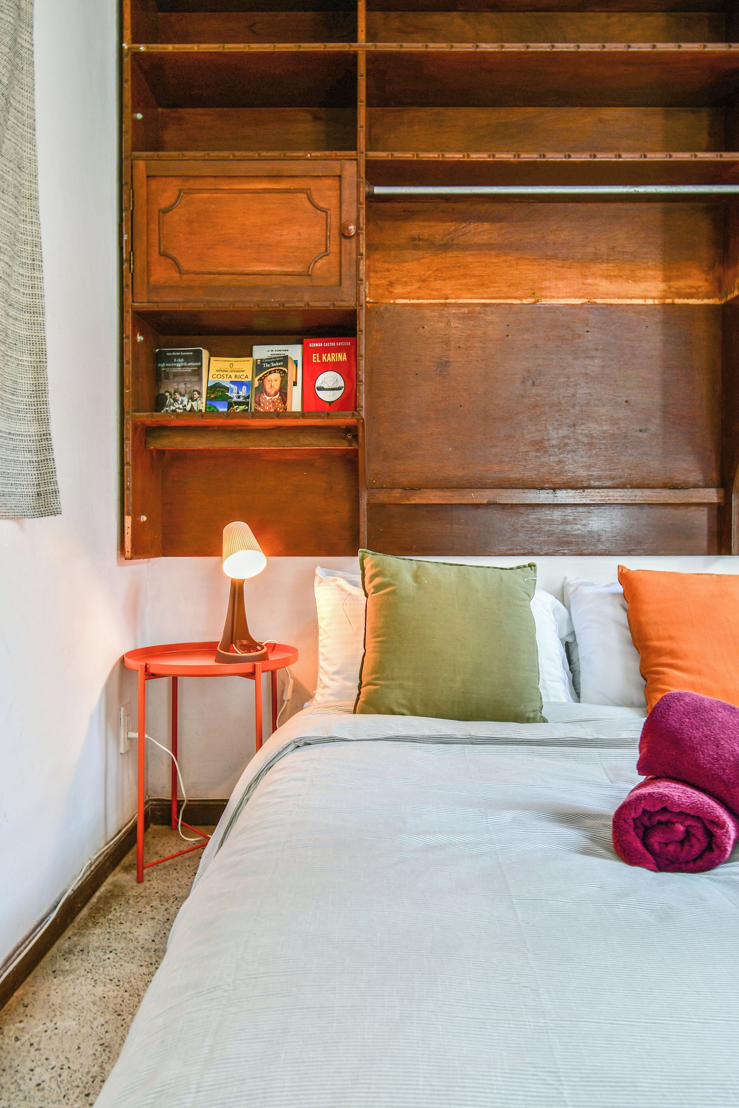 Une chambre à coucher avec un lit, des oreillers, une table de chevet, une lampe et une armoire en bois.
